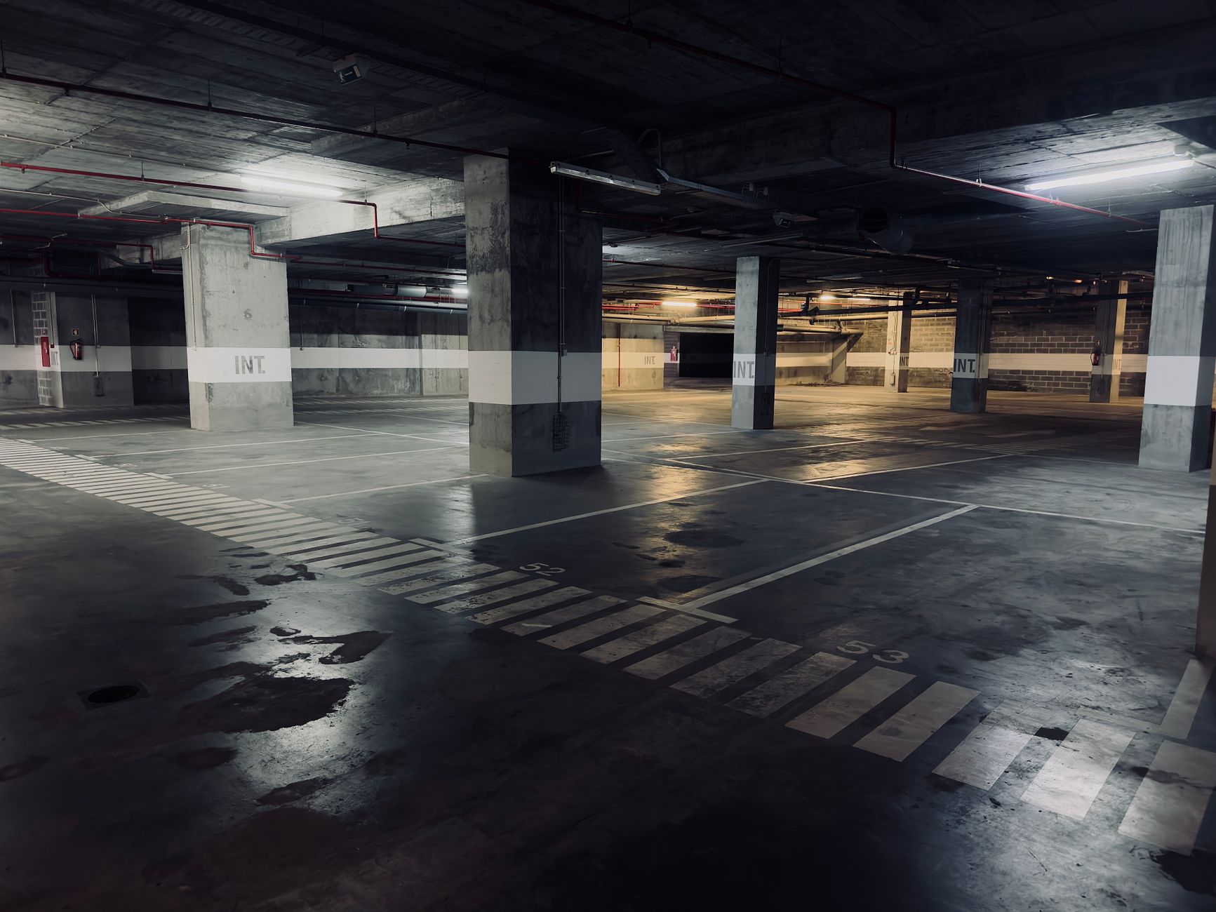 A moody underground parking garage featuring empty spaces and puddles on the floor