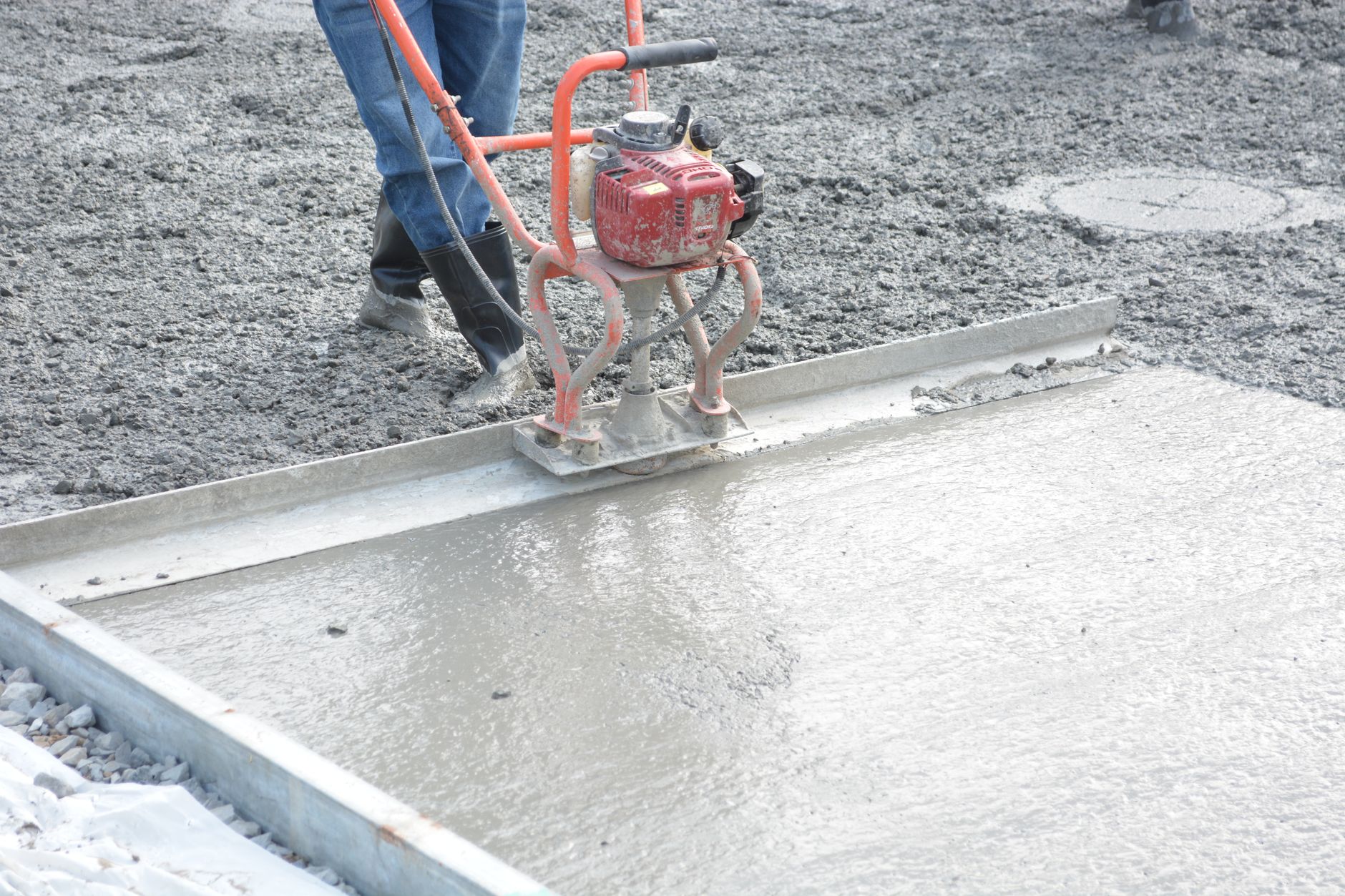 A construction worker operates a power trowel to smooth freshly poured concrete on a construction site