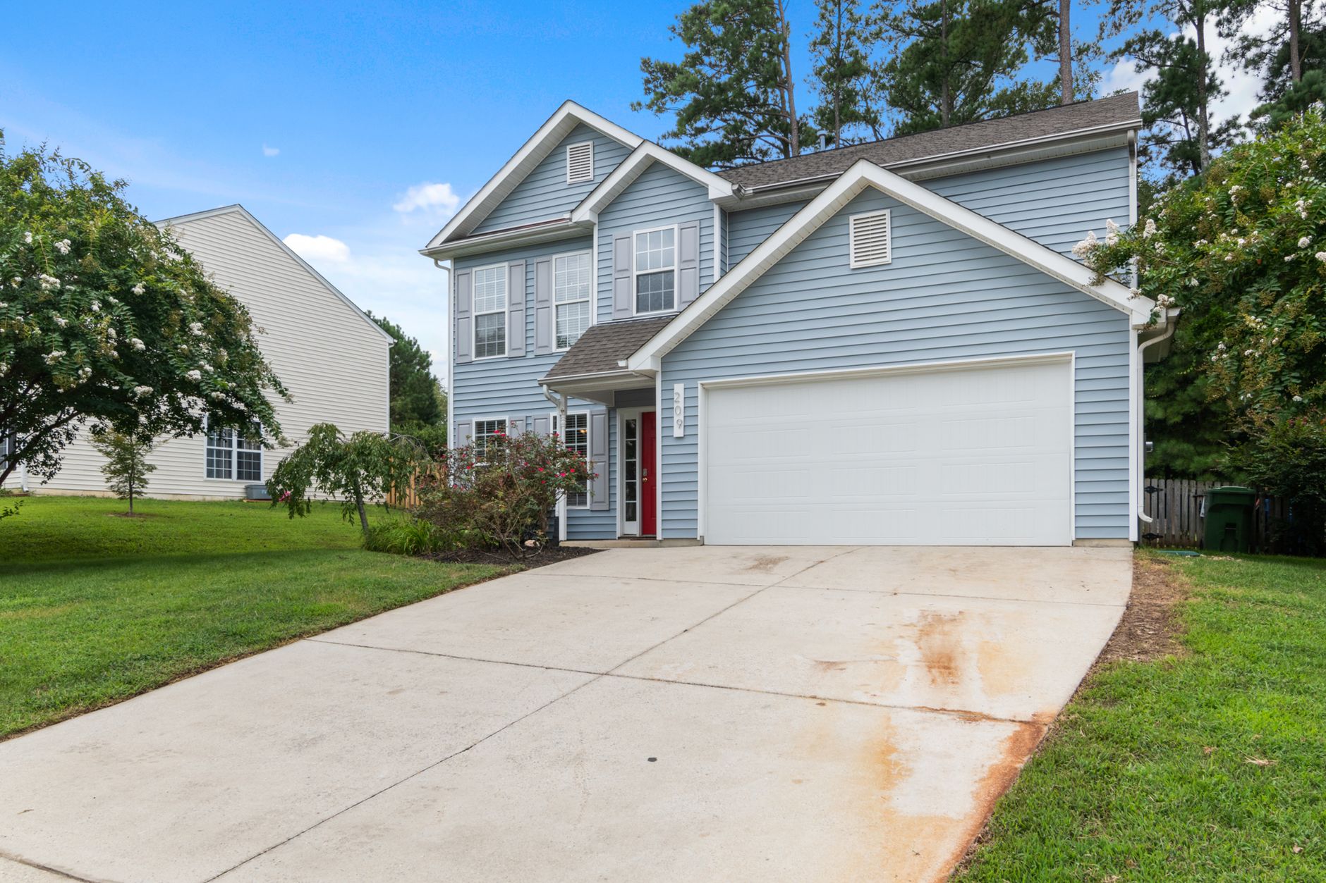 Charming two-story suburban house with spacious driveway and greenery.