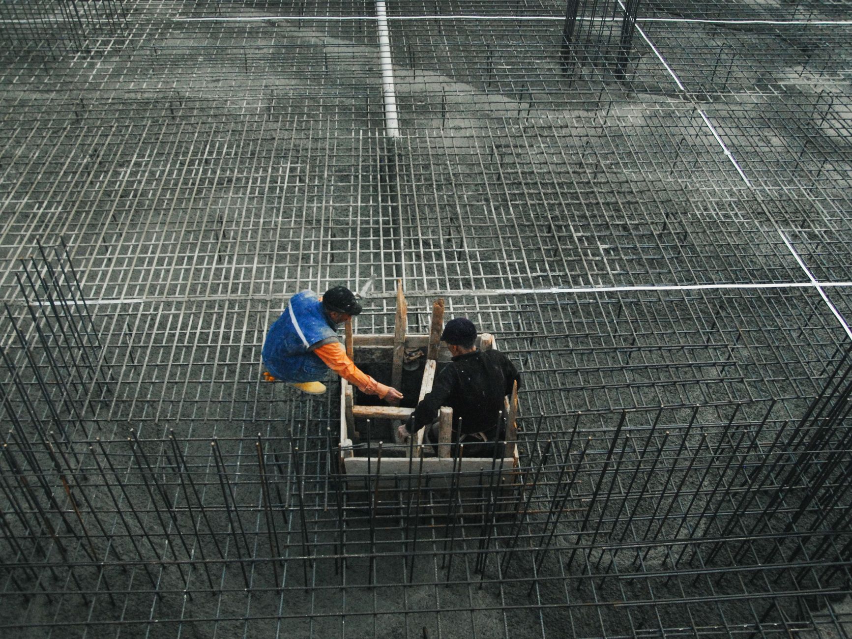 Two workers operating on a construction site with steel frameworks and concrete. High-angle view captures teamwork and industry