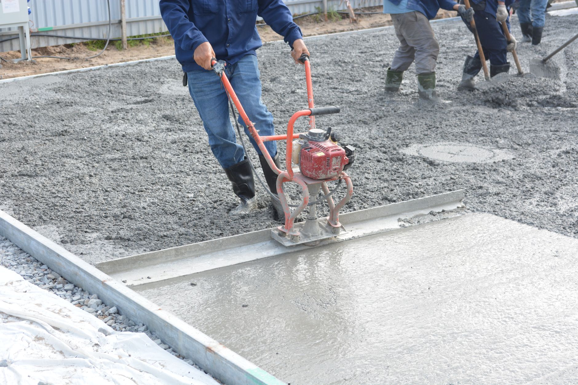 Team of construction workers using power tools to level freshly poured concrete on a building site